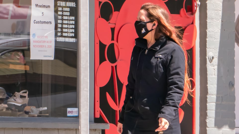 Une femme masquée se promène devant une vitrine de magasin.