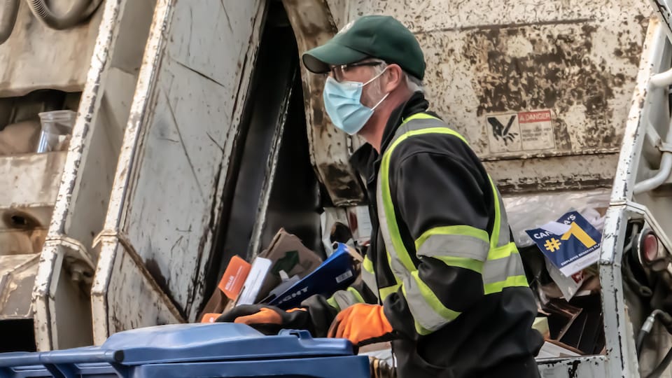 Un employé du service d'entretien de la Ville ramasse un bac de recyclage.