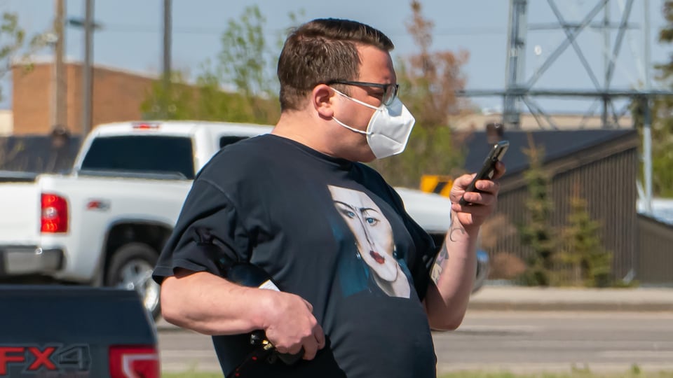 Un homme portant un masque regarde son téléphone dans la rue.