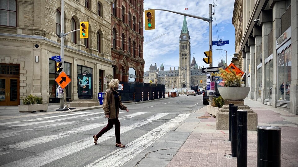 Une personne portant le masque traverse une rue d'Ottawa, avec le parlement en fond.