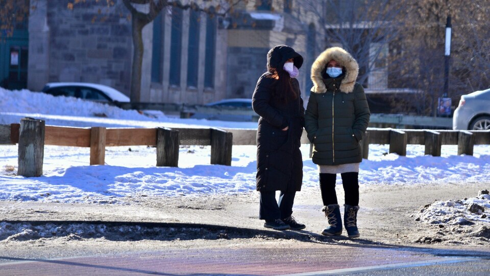 Des femmes qui portent un masque discutent sur un trottoir.