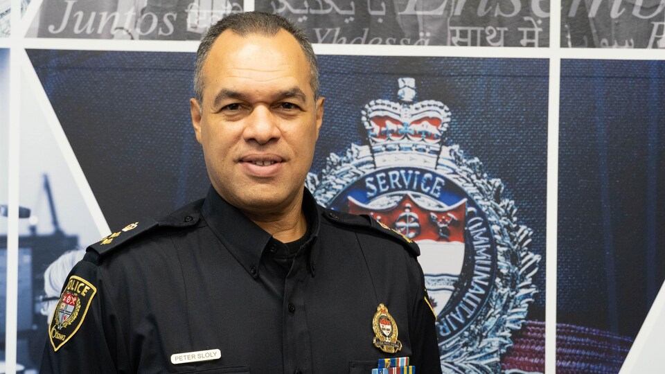 Peter Sloly pose devant le logo du Service de police d'Ottawa