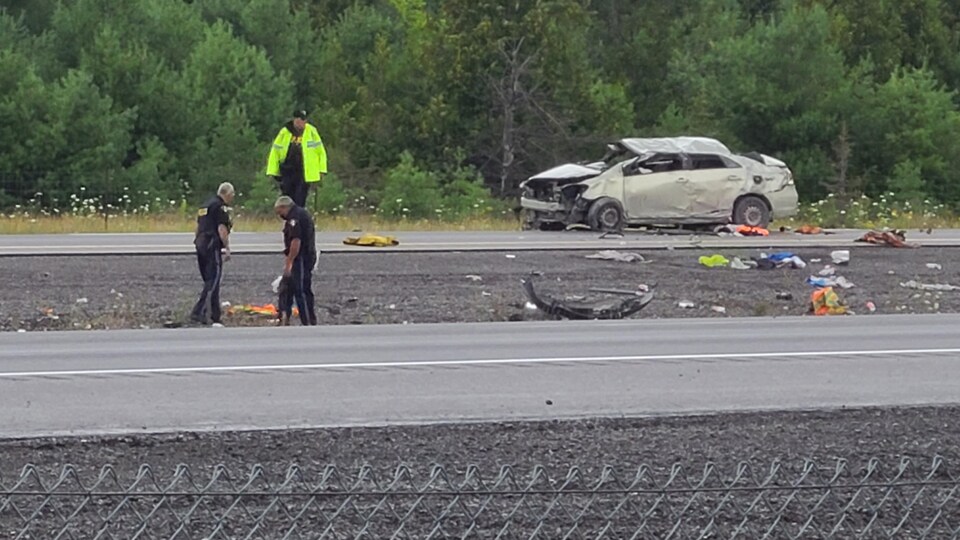 Trois policiers regardent les débris sur la chaussée, près du véhicule accidenté.