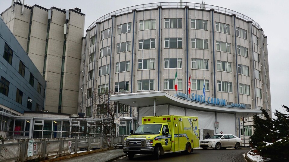 L'entrée de l'hôpital à la forme arrondie, devant laquelle est stationnée une ambulance.