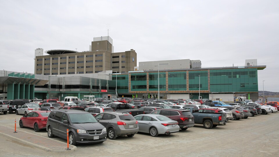 Un hôpital et un stationnement rempli de voitures. 