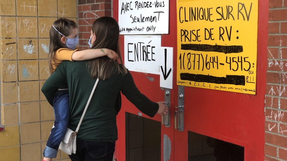 Un enfant dans les bras d'une femme près d'une porte d'entrée.