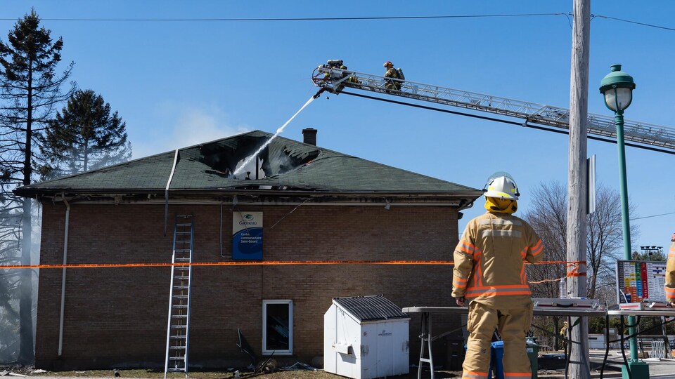Des pompiers arrosent un toit en flamme.