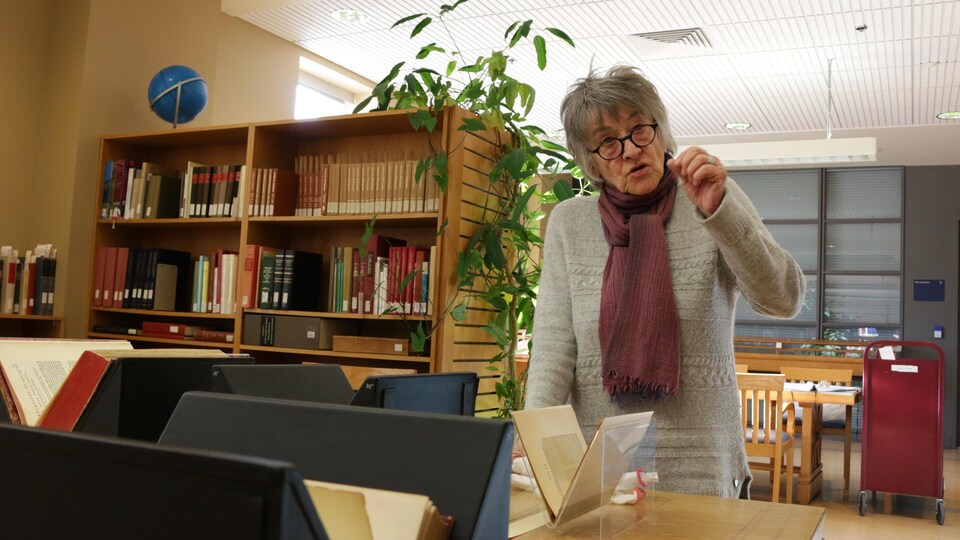 Une femme explique des nuances de la langue innue devant des livres anciens en langue innue.