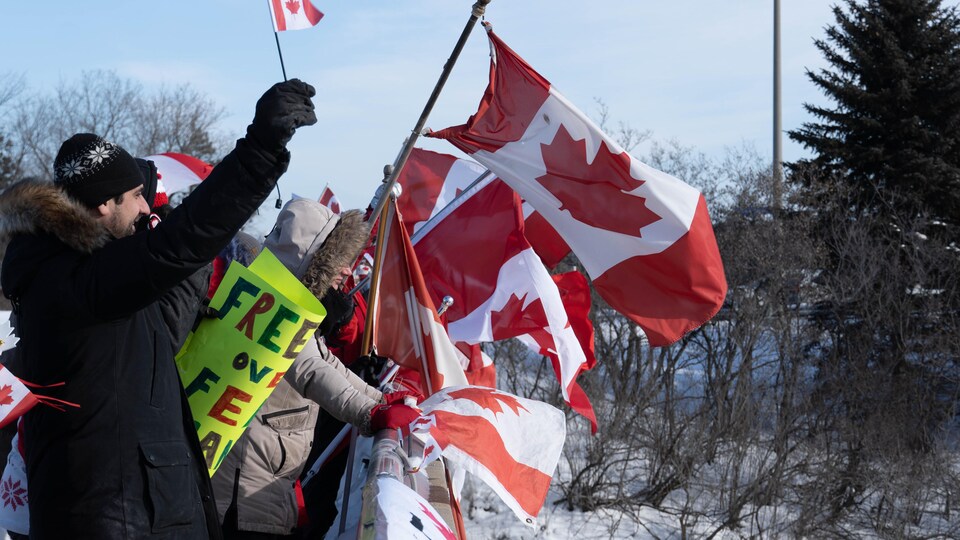 Des gens brandissent le drapeau canadien et des pancartes en hiver.