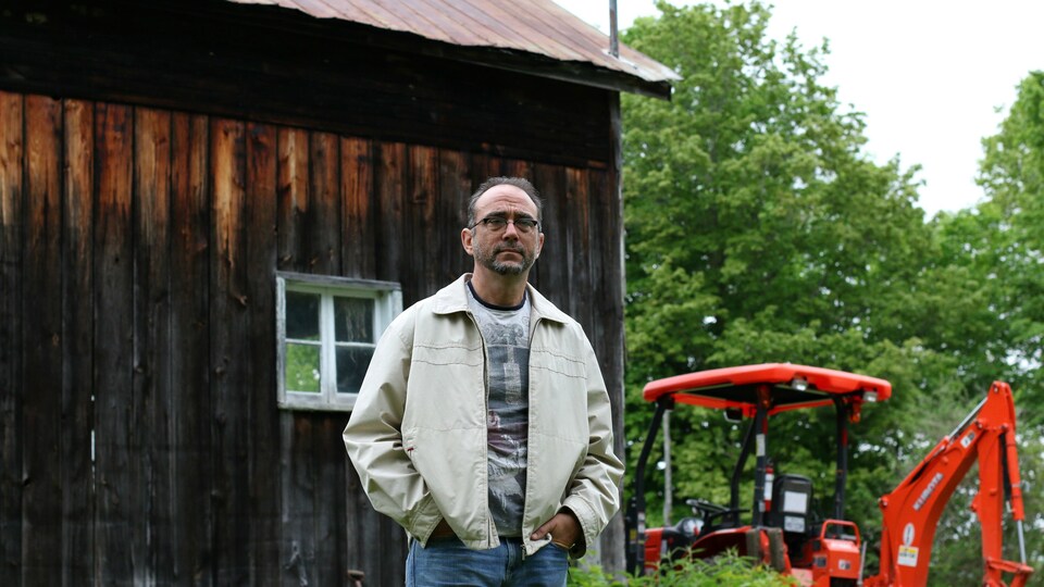 Stéphane Gendron pose devant un bâtiment agricole et un tracteur.