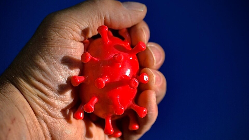 Plan rapproché d'une main qui presse une balle antistress rouge qui représente un virus.