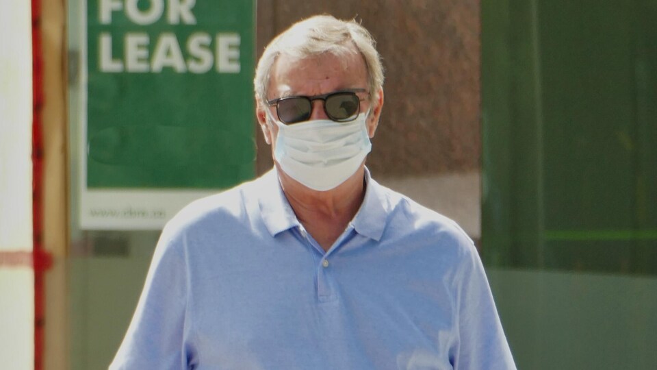 Un homme portant un masque et des lunettes fumées dans une rue de Regina.