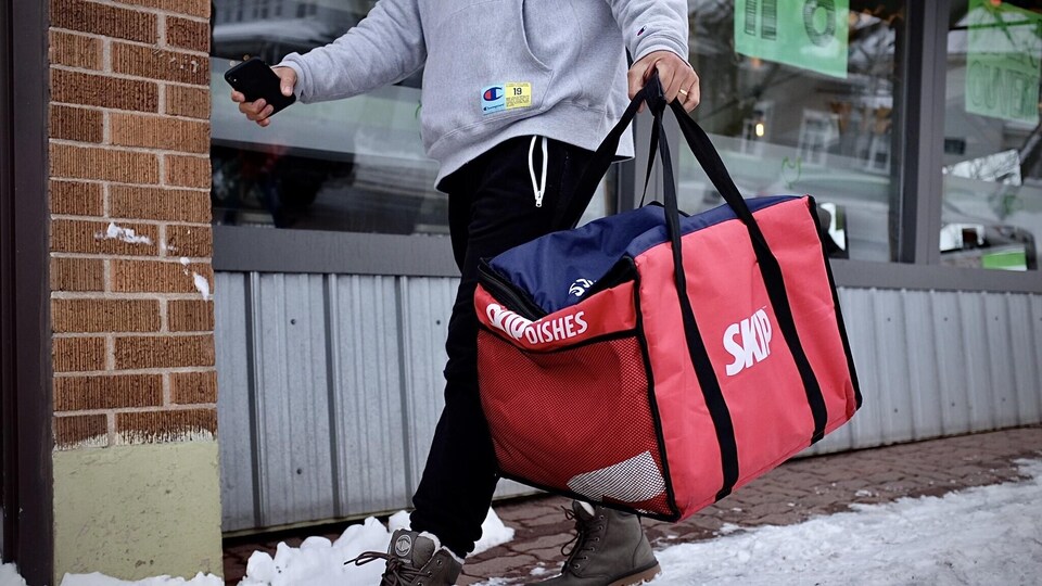 Un livreur de SkipTheDishes marche dans une rue avec un sac de livraison.