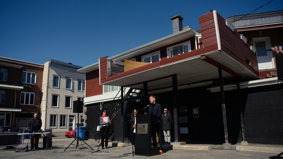 Le maire Bruno Marchand derrière un micro et devant le bâtiment du bar Le Kirouac.
