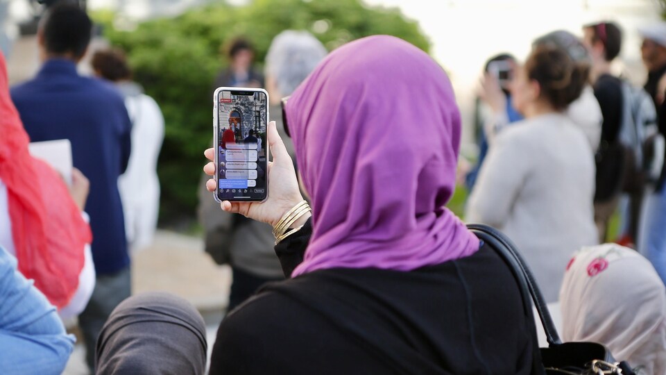 Une femme voilée de dos tient son téléphone dans une foule.