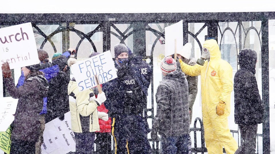 Des policiers au milieu de manifestants brandissant des pancartes devant l'hôtel de ville de Moncton.