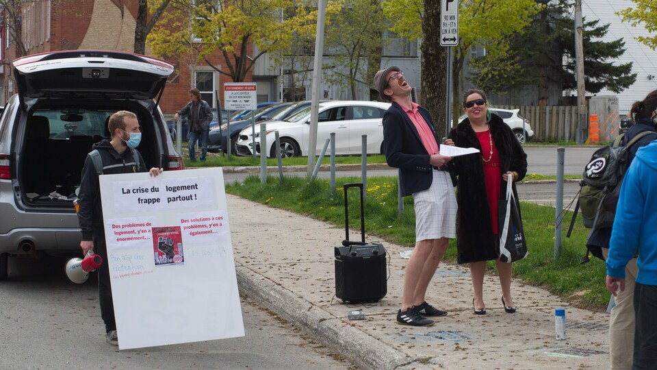 Un manifestant tient une affiche et un porte-voix et deux autres sont déguisé en « riche ».