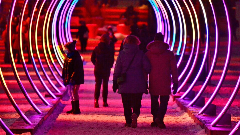 Des personnes marchent dans un tunnel formé d'anneaux lumineux, dans une rue de Montréal.