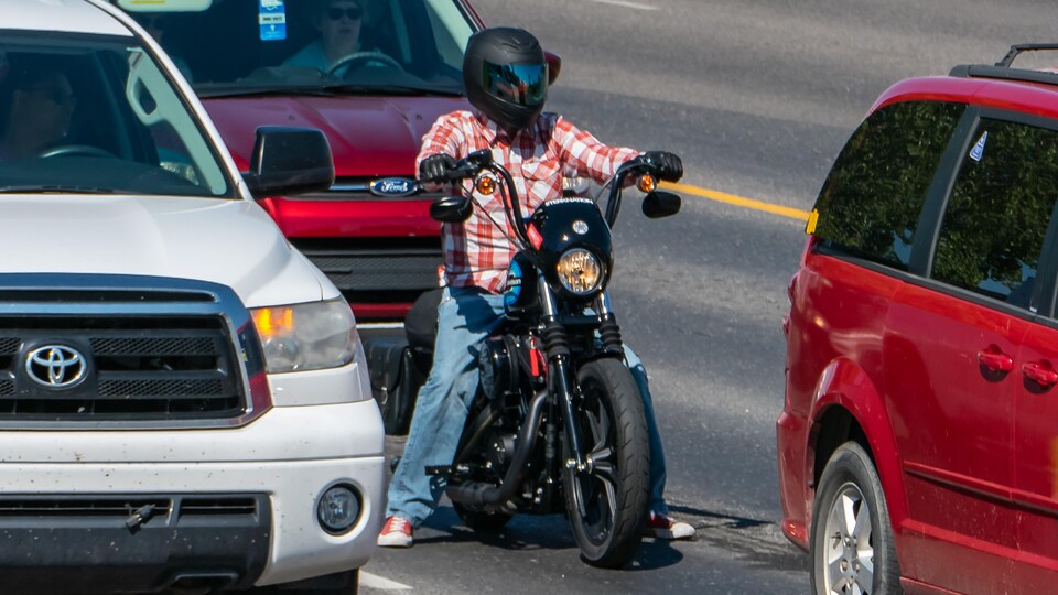 Un motocycliste immobilisé attend de démarrer entre deux voitures.