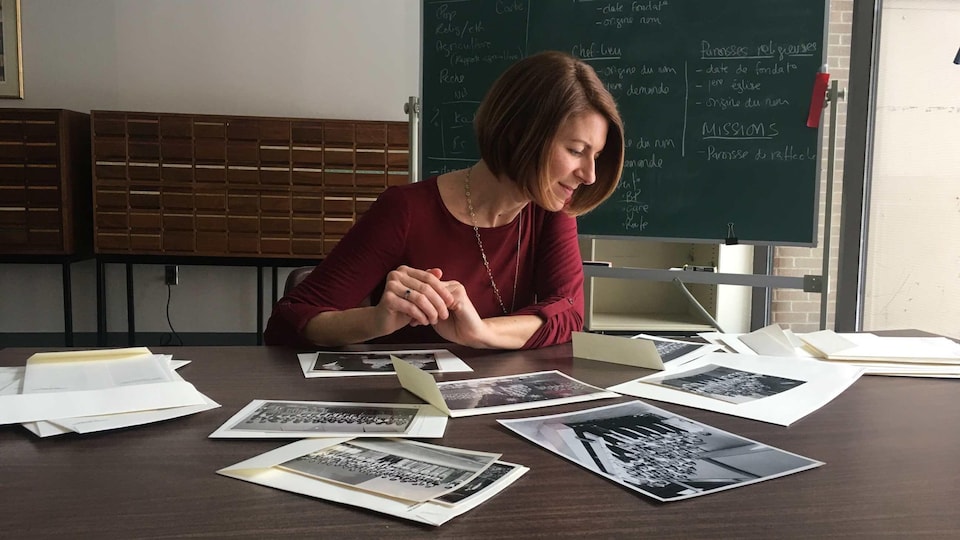 Nadine Hébert est assise derrière une table et regarde des photographies d'archives.