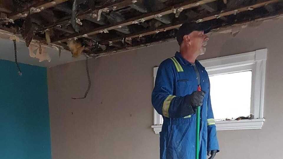 Un homme vêtu d'une combinaison de chantier balaie des débris dans une maison.