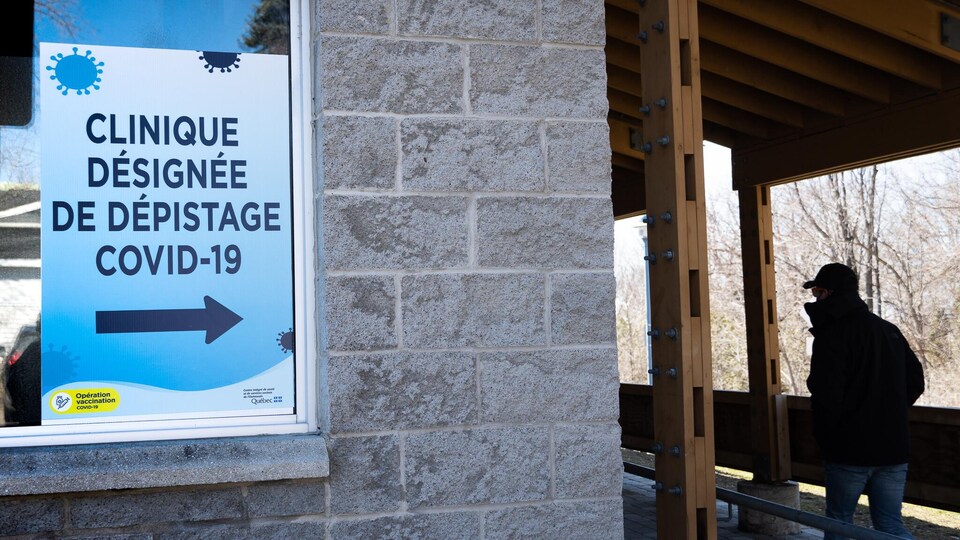 Un résident, dans l'ombre, marche près d'une affiche sur laquelle on peut lire « clinique désignée de dépistage covid-19».