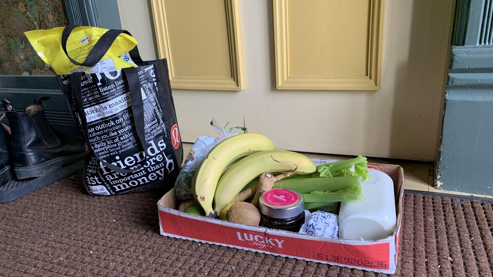 Un carton et un sac d'épicerie sont déposés devant une porte fermée.