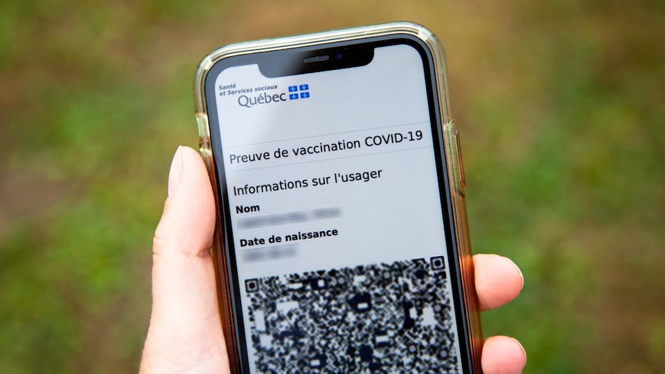 Quelqu'un tient un téléphone intelligent. On aperçoit la preuve vaccinale sur l'écran.