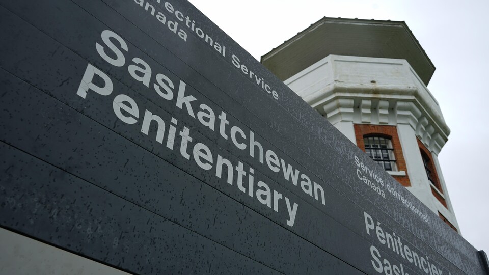 Un panneau sur lequel est écrit Pénitencier de la Saskatchewan. Derrière, on voit une tour du pénitencier. 