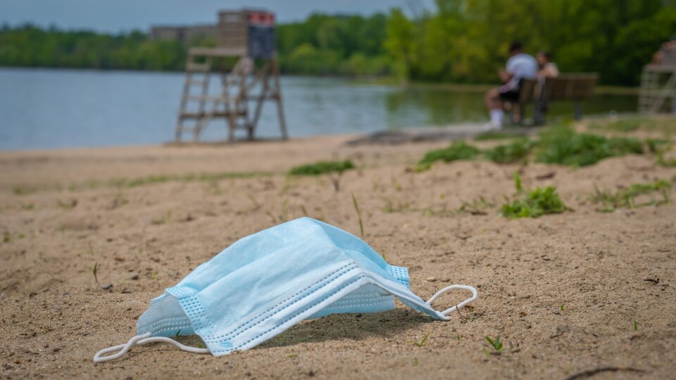 Un masque chirurgical sur le sable, près d'un plan d'eau.