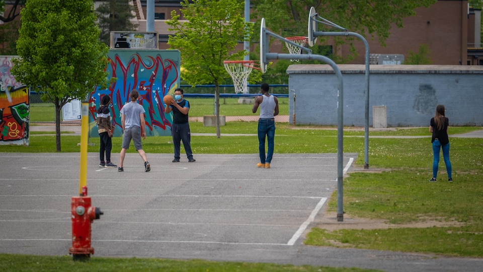 Quatre personnes dont une portant un masque, jouent au basketball à l'extérieur.