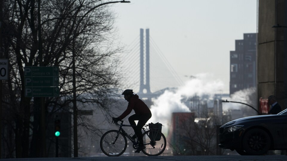 Une personne passe en vélo dans la rue. Au loin, de la fumée émane d'une bâtisse.