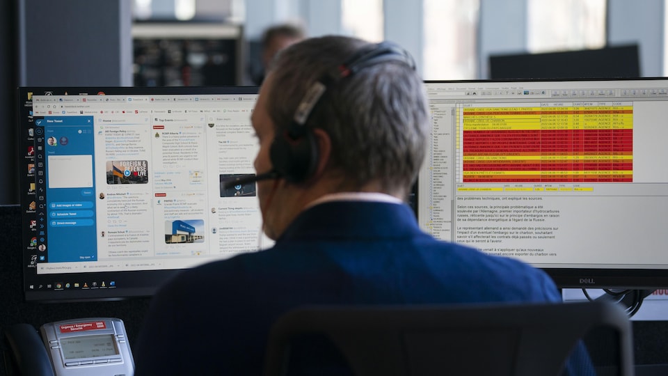 A journalist, seen from behind, sitting in front of computer screens in a newsroom.