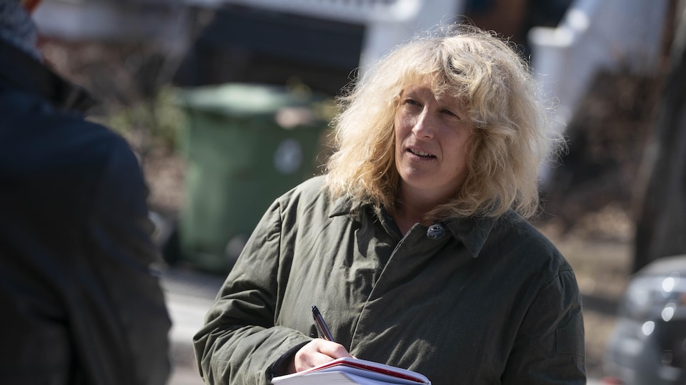 A journalist, holding a notebook, listens to someone at an outdoor lecture.