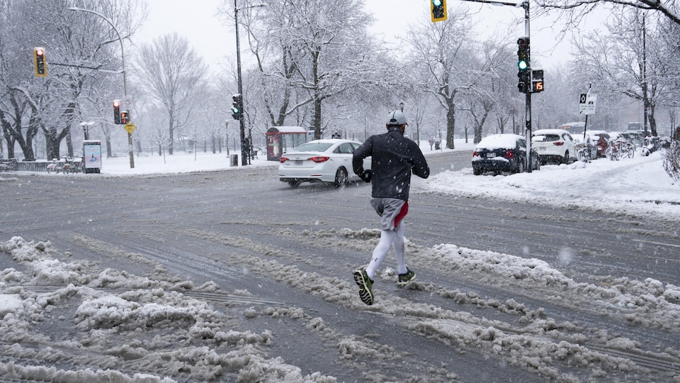 Un piéton court en traversant une rue jonchée de neige.