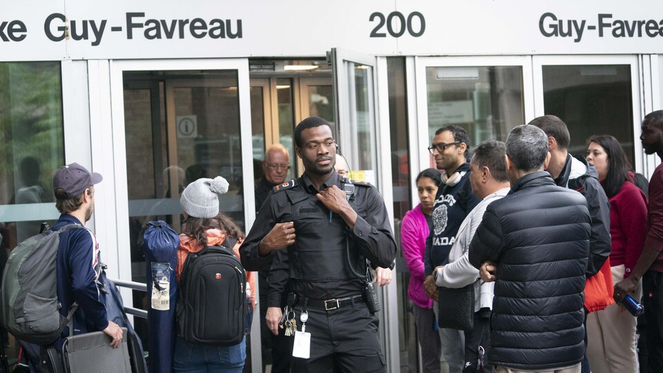 Un agent de sécurité est debout au milieu de nombreuses personnes agglutinées devant l'entrée du Complexe Guy-Favreau, à Montréal.