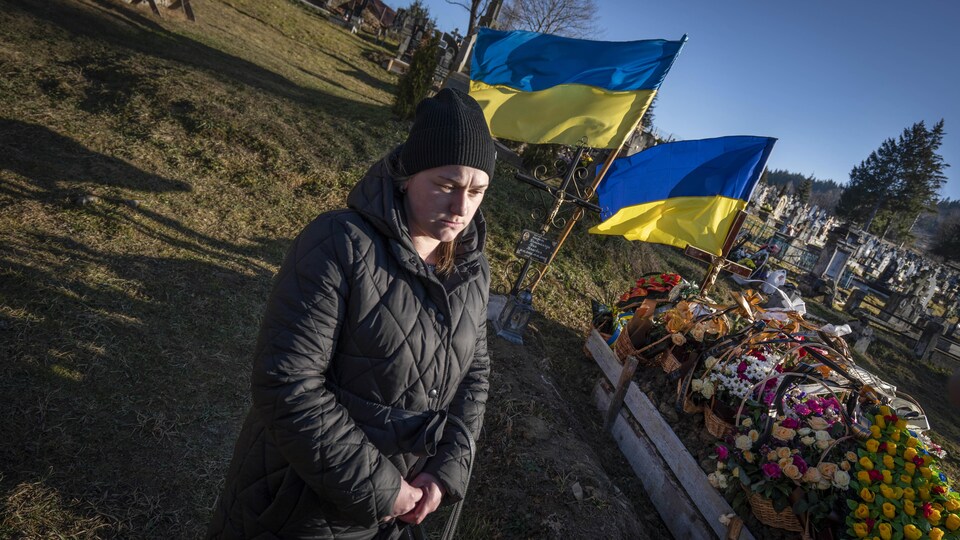 Des fleurs surmontées de drapeaux ukrainiens ornent une tombe.