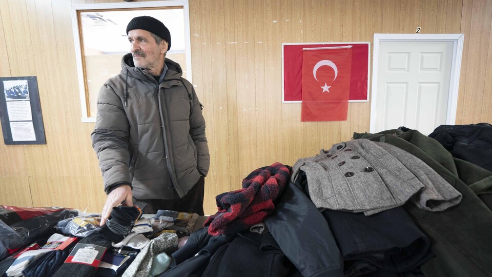 Portrait de Mehmet Sozen, debout derrière une table sur laquelle des vêtements sont déposés.