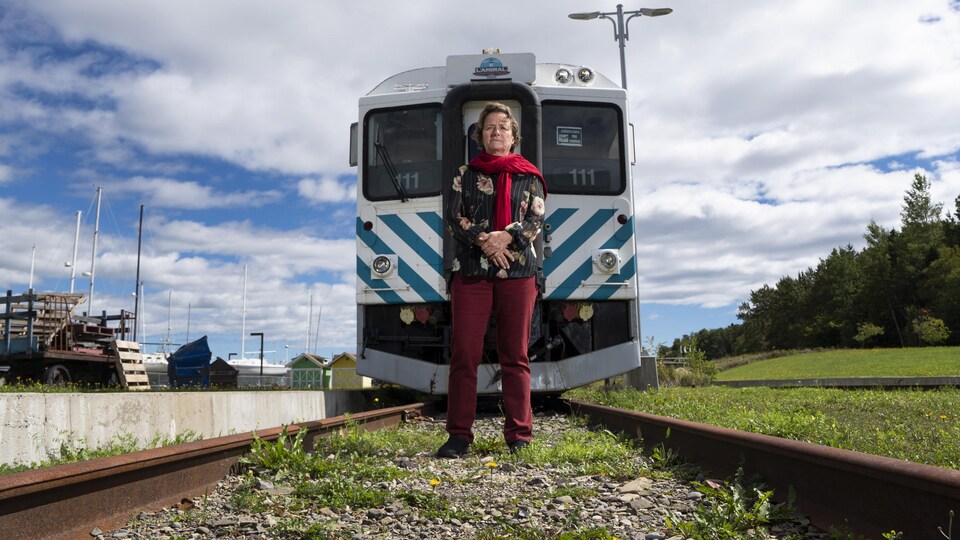 Elle est devant un train, au milieu des rails.