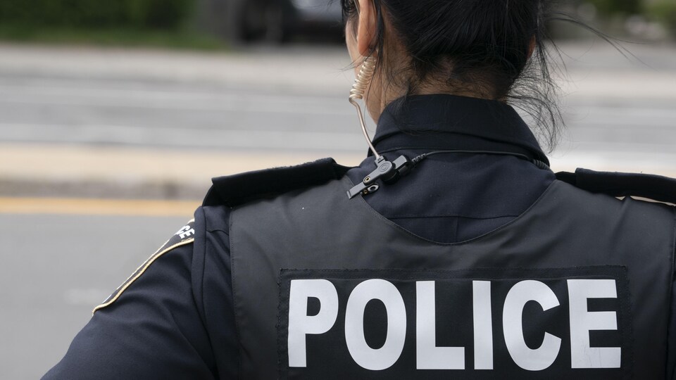 Une policière, de dos, porte un dossard sur lequel il est inscrit « police ».