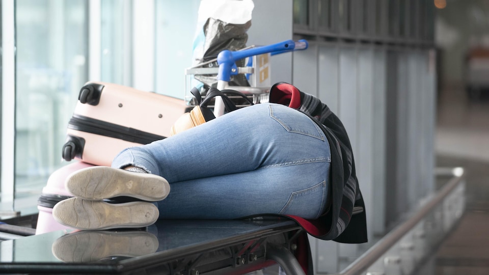 Une voyageuse attend son vol à l'aéroport Trudeau de Montréal, allongée sur un banc.