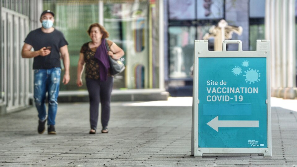 Un homme portant un masque et une femme marchent côte à côte près d'un centre de vaccination contre la COVID-19.