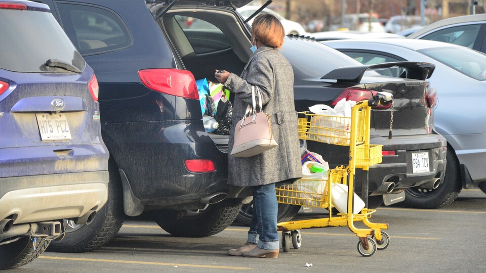 Une femme range son épicerie dans la valise de sa voiture.