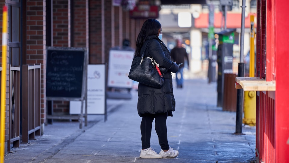 Une personne avec un masque et un cellulaire à la main sur le trottoir du centre-ville d'Ottawa.
