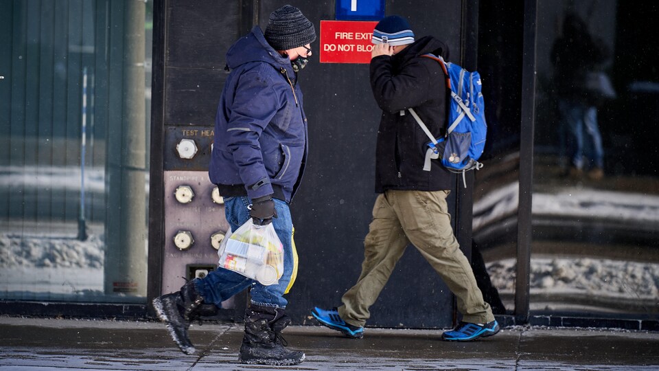 Deux hommes avec un masque se croisent sur un trottoir d'Ottawa.