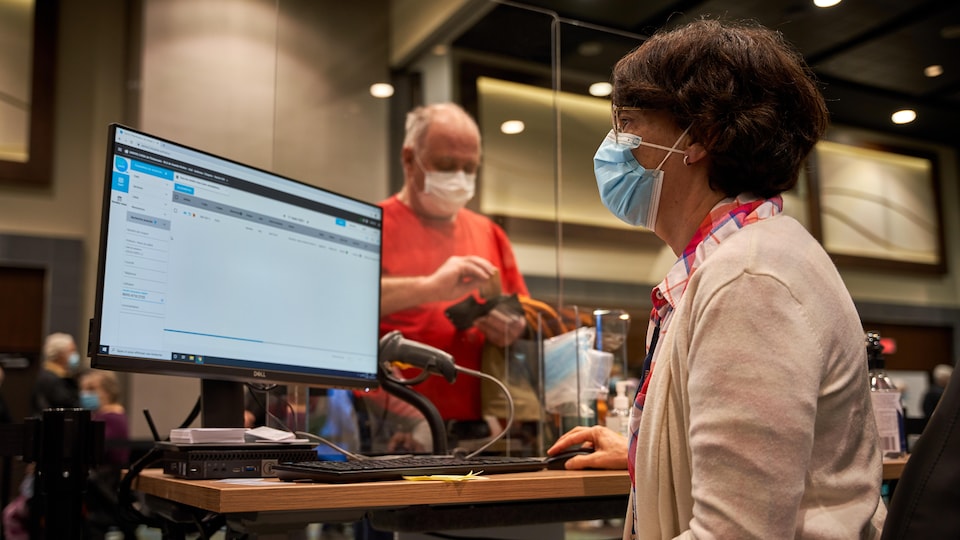 Une femme devant un écran d'ordinateur enregistre un patient pour la vaccination.
