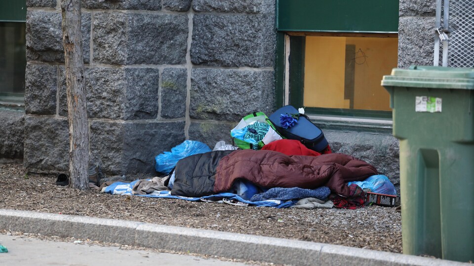Ein Schlafsack und Habseligkeiten eines Obdachlosen liegen auf dem Boden in der Nähe einer Steinmauer.