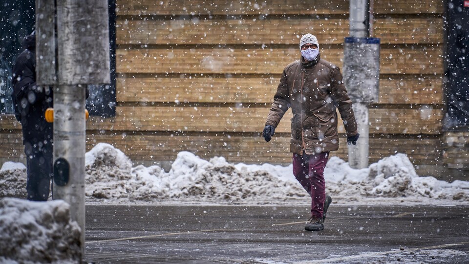 Un piéton masqué traverse une rue d'Ottawa pendant une averse de neige.