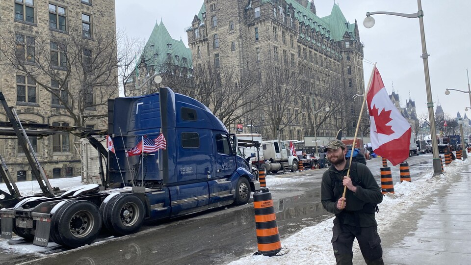 Un homme porte un drapeau du Canada devant des camions stationnés.