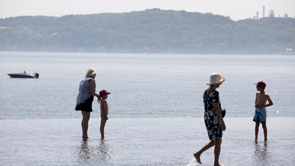 People with their feet in the water at the new swimming pool on the Promenade Samuel-de-Champlain.